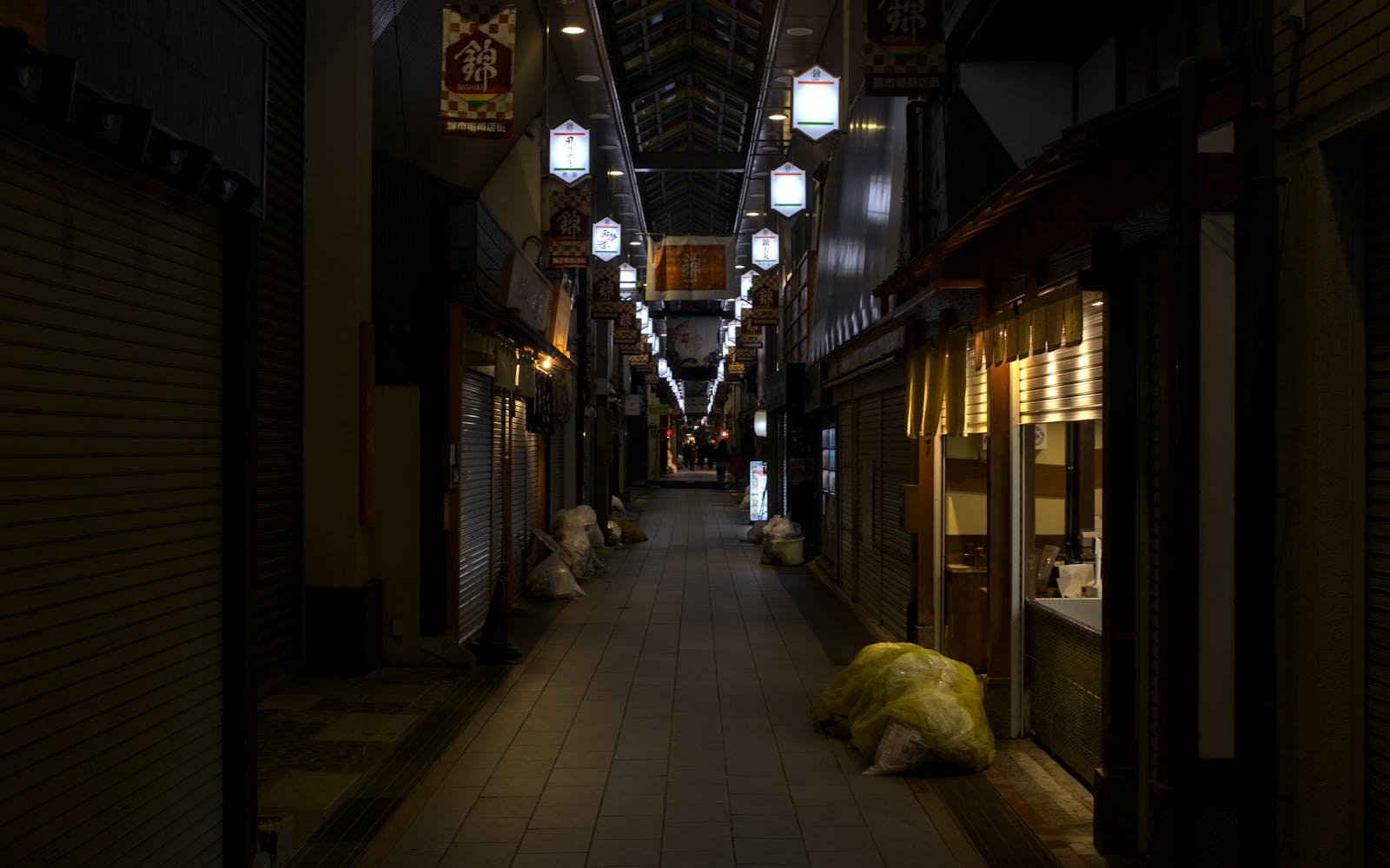 A long, narrow alleyway lined with brick walls and scattered debris, leading to an unseen destination.